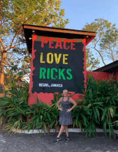 the Hostel Mom standing in front of Rick's cafe sign in Negril Jamaica