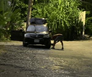 Driver changing flat tire on side of road 